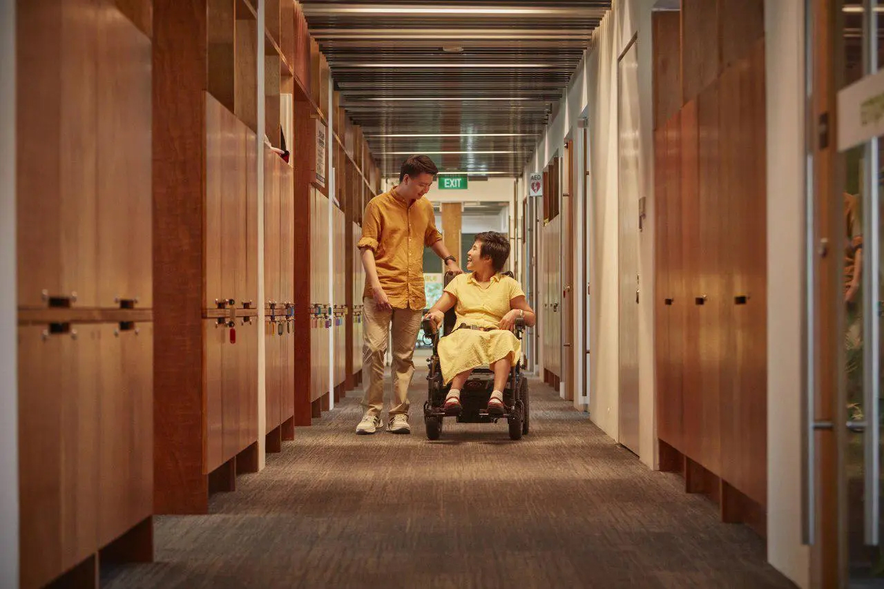 An SG Enable colleague walking alongside a wheelchair user in an office corridor